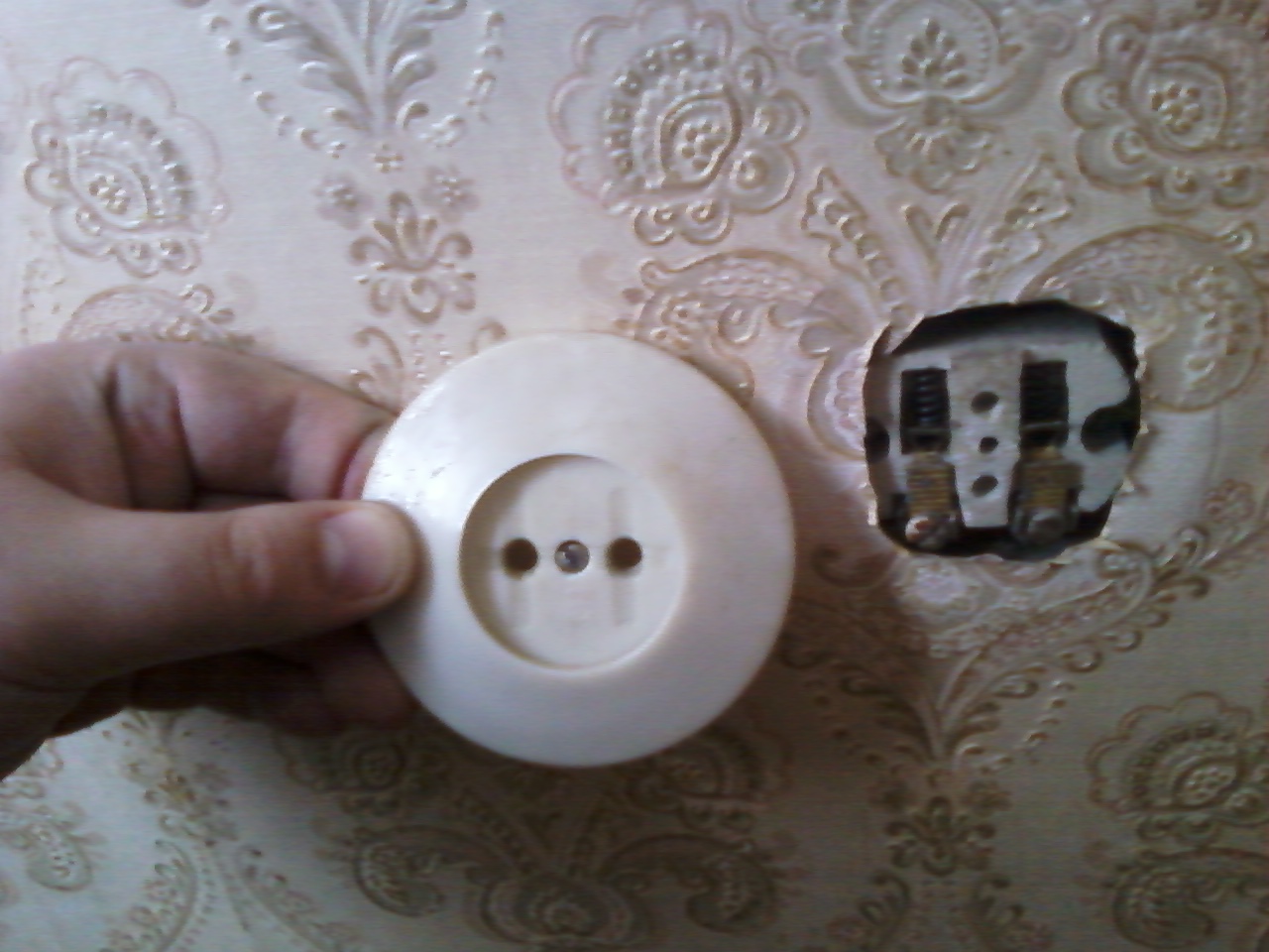The cover removed from an old two-hole socket, with the recess in the wall and two terminals beside it