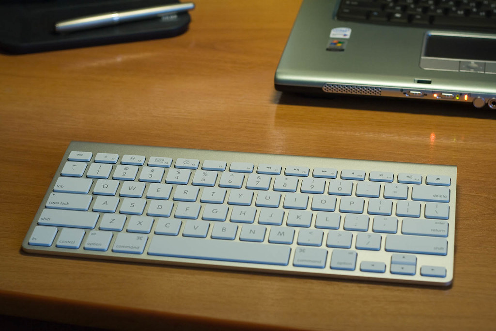 A wireless keyboard on a desk, the edge of a laptop beside it