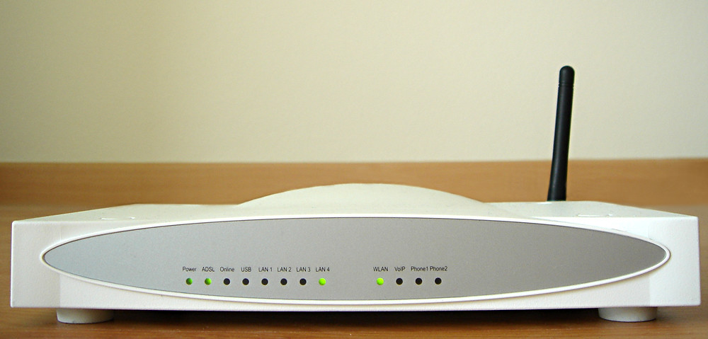 A Wi-Fi router with a single antenna on a table, a row of indicator lights on the front panel