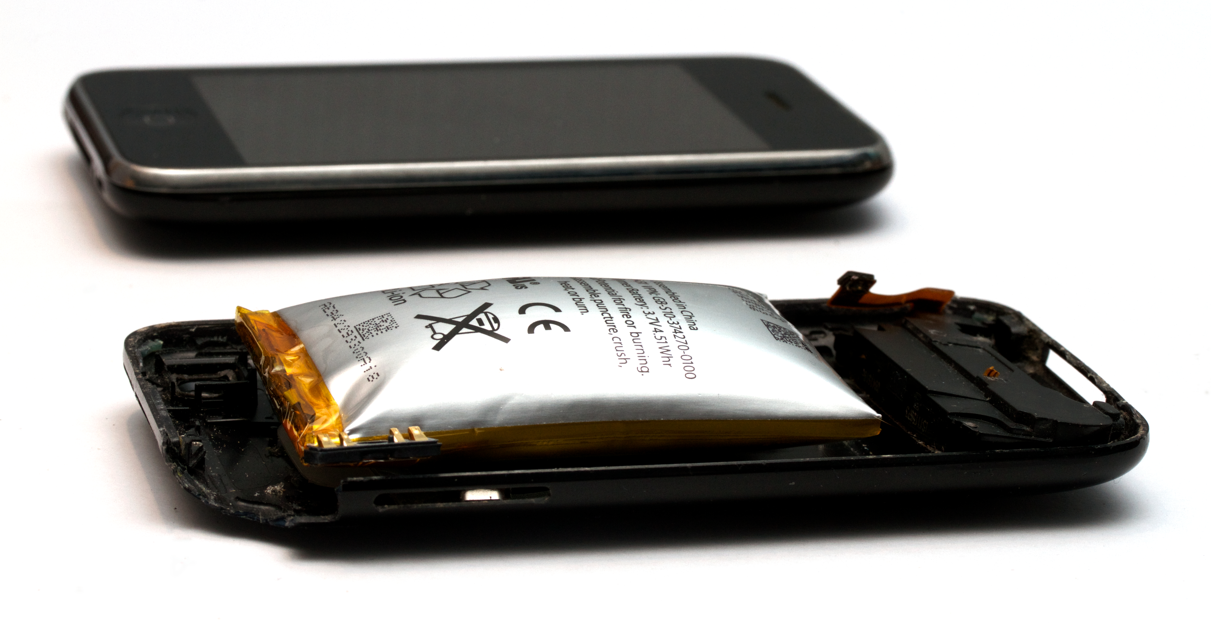 An opened smartphone with a swollen battery bulging out of it; a second handset lies on the table nearby