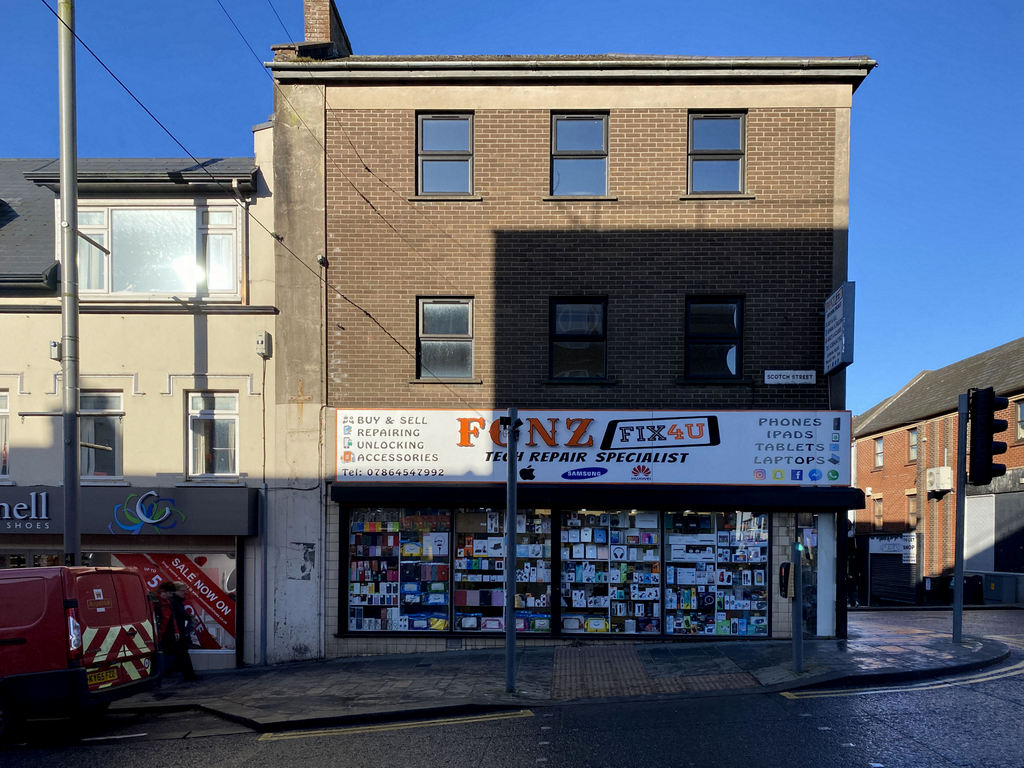 A phone repair shop front on a street corner; the sign lists repairs to phones, tablets and laptops