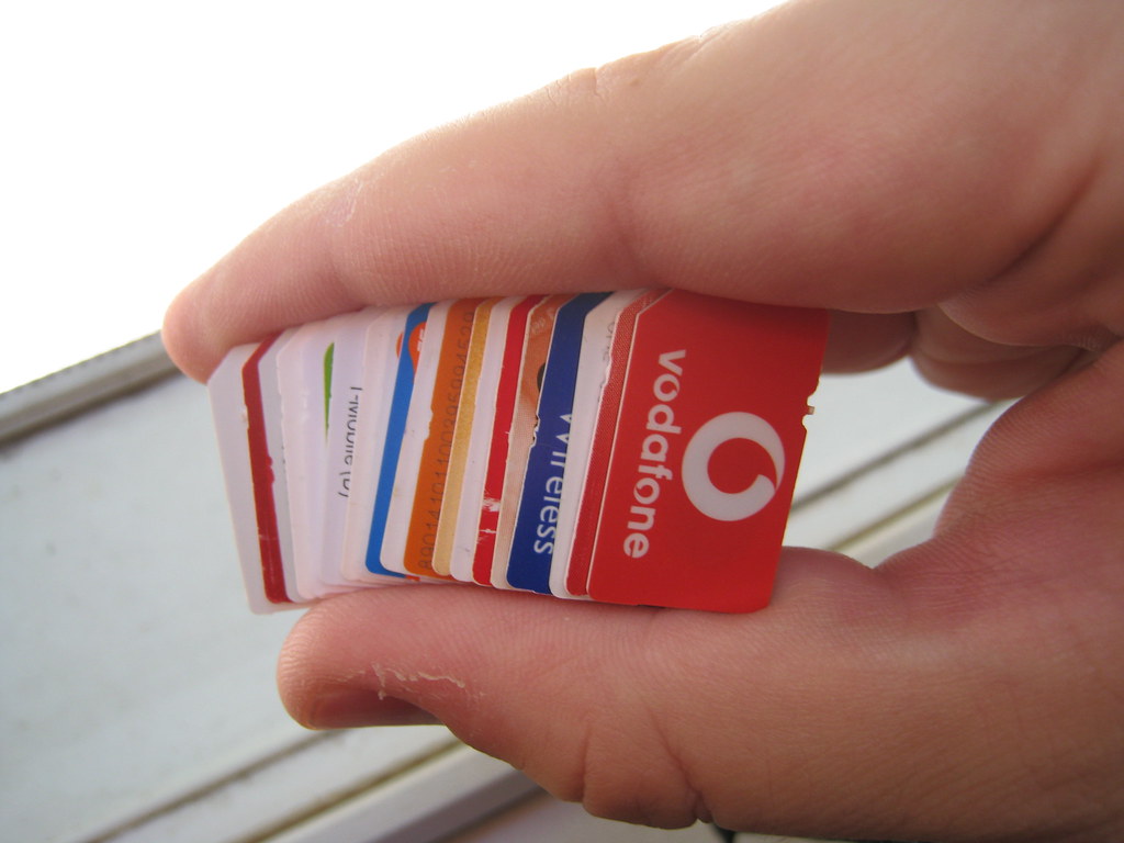 A hand holding a fanned-out stack of SIM cards from different operators.