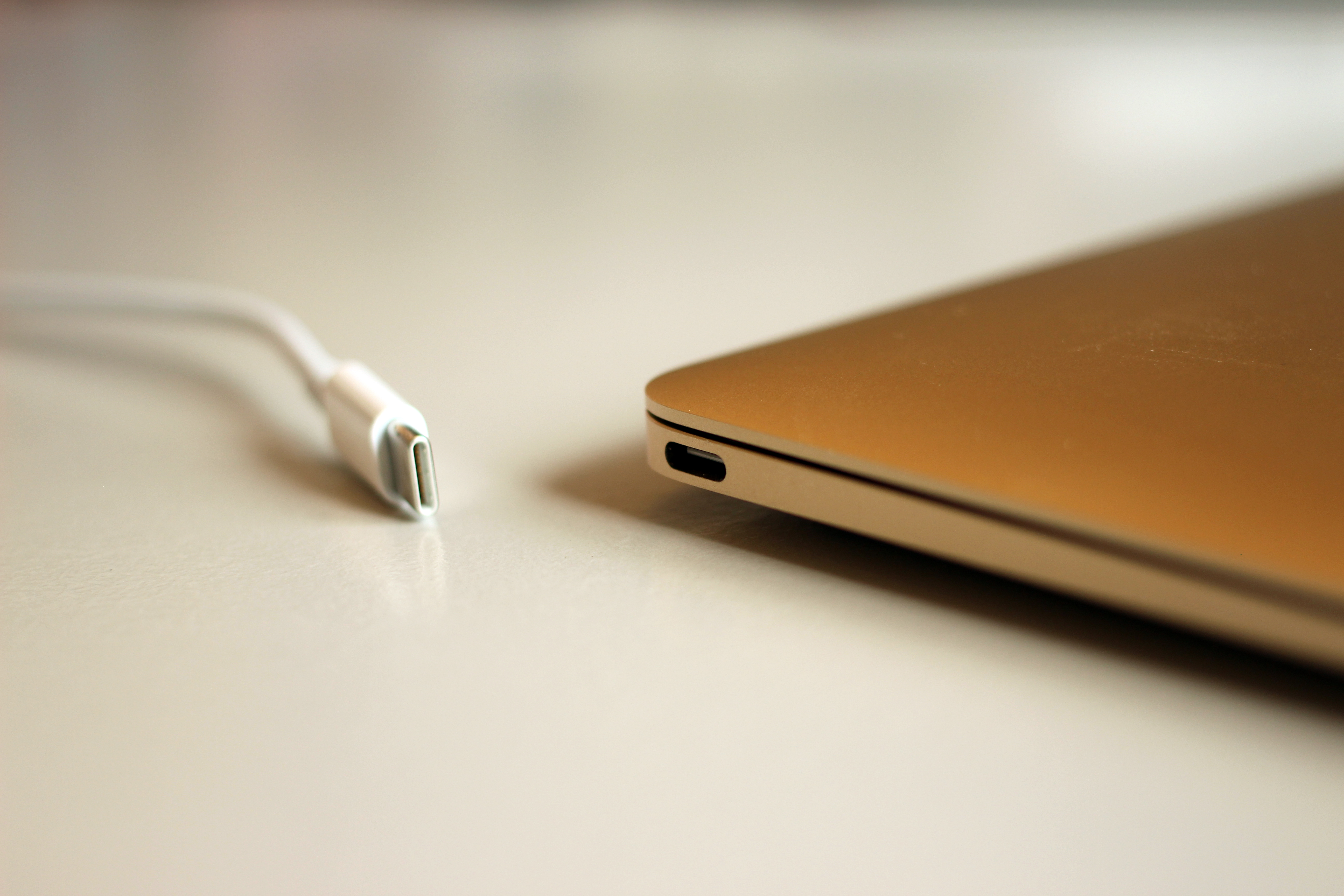 A thin laptop seen edge-on with a single USB-C socket and a cable lying beside it