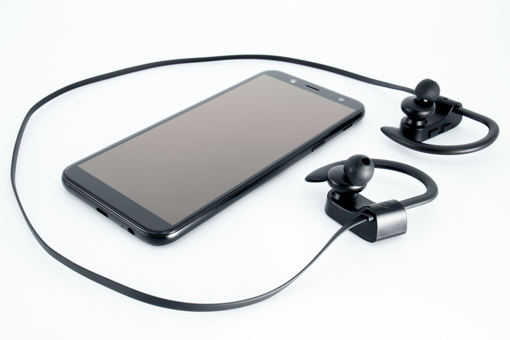 A smartphone and a pair of wireless in-ear headphones on a white background